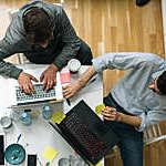 Young entrepreneurs working in their start-up office. They are talking and using laptops. Coding. Overhead view.