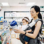 Young Asian mother carrying cute baby girl shopping for baby product in a shopping mall and is looking at a variety of baby formula