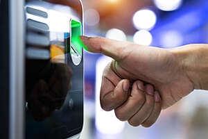 Close-up of a woman approaching her thumb to a biometric fingerprint reader.